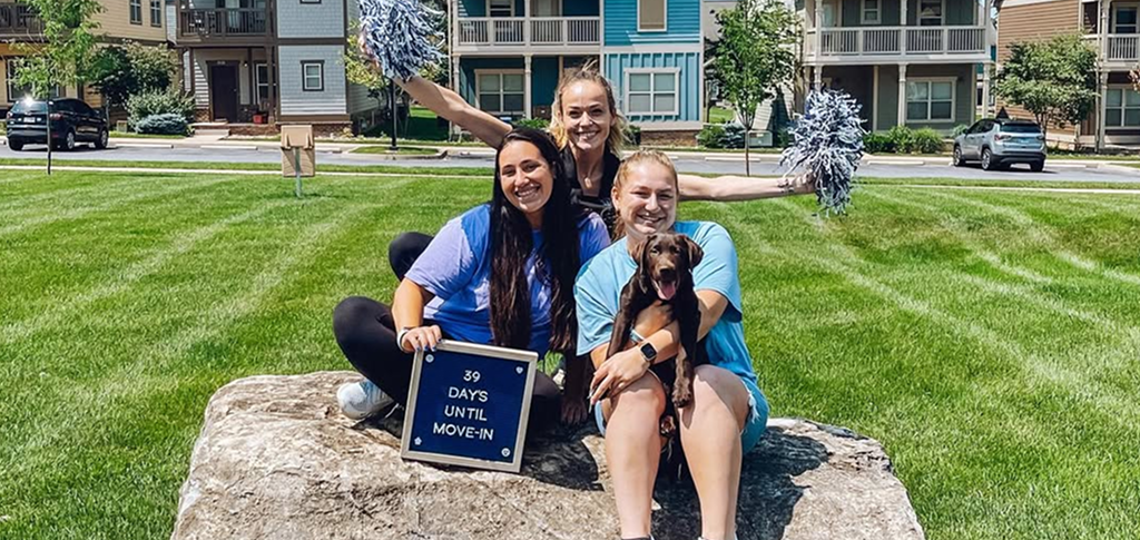 three young women with a puppy sitting on top of a rock, holding a sign that says 39 days until move-in