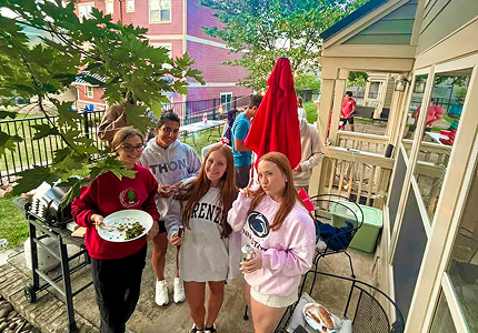 four young women posing for the camera outdoors near a grill